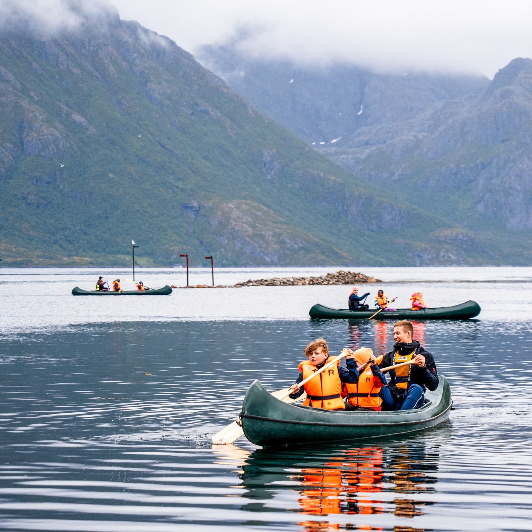 Tre kanoer på speilblank fjord med dramatiske fjell