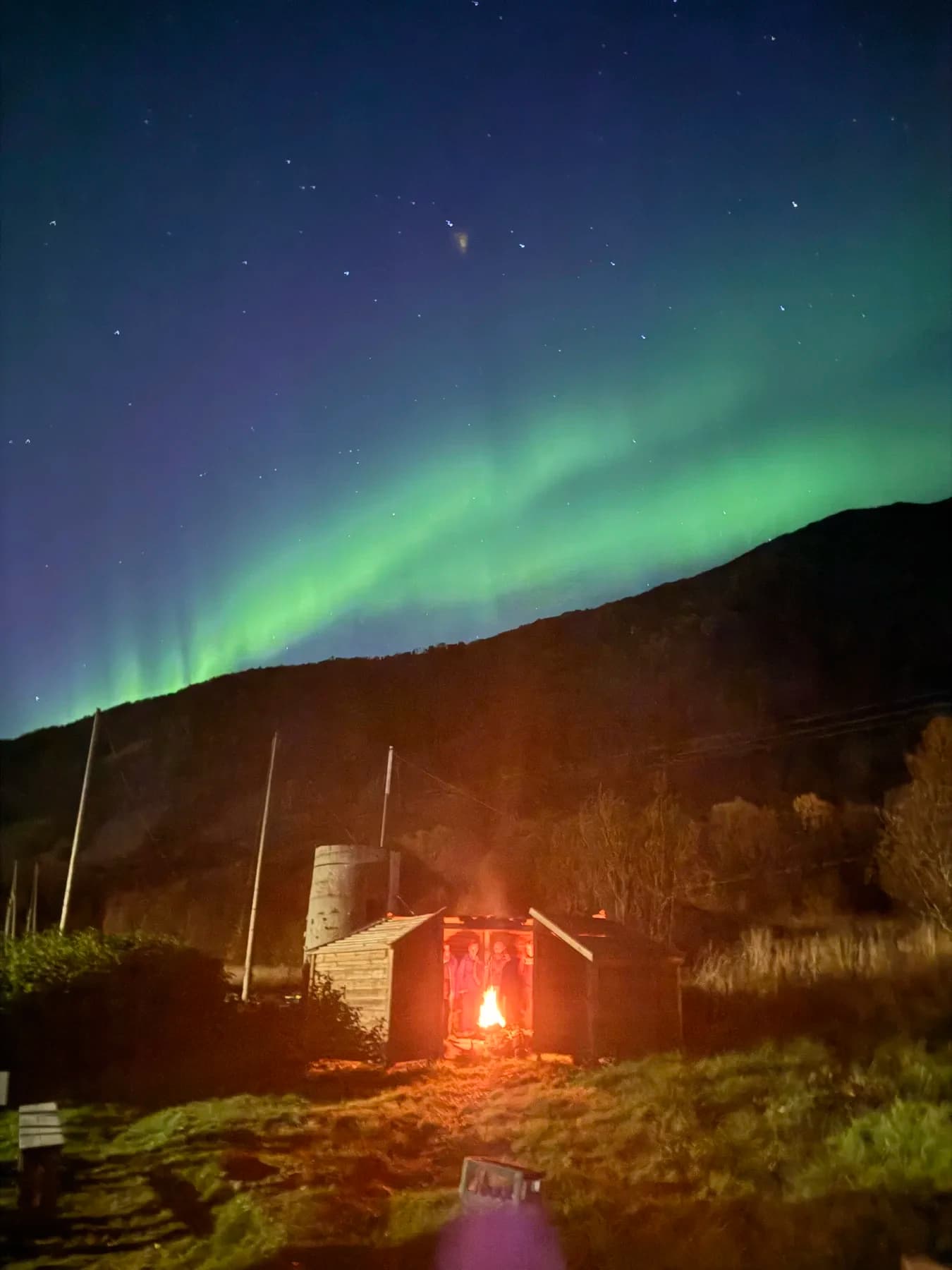 Nordlys over åsen med bålglød ved gapahuken