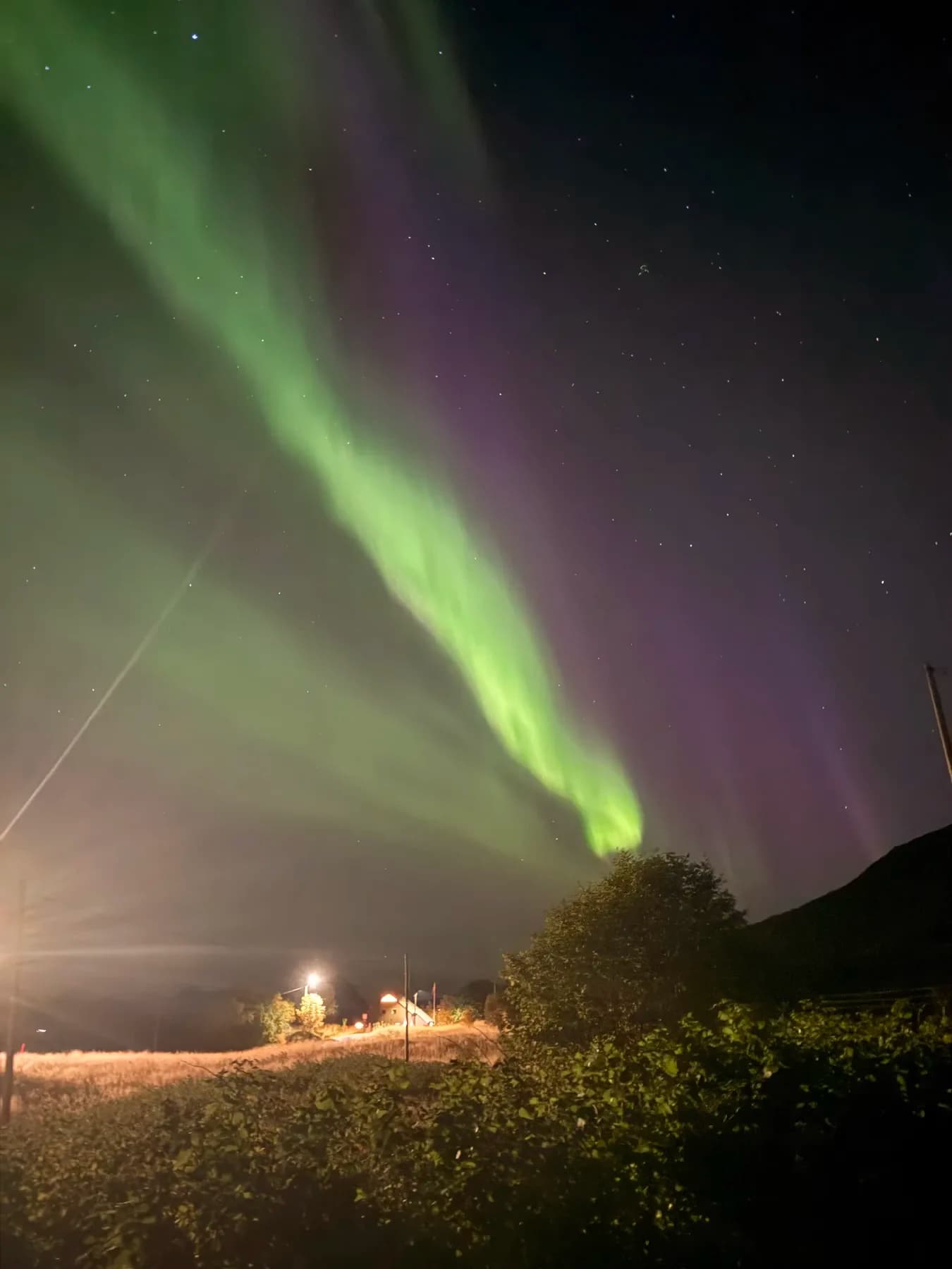Nordlys over kystlinjen med fjerne lys