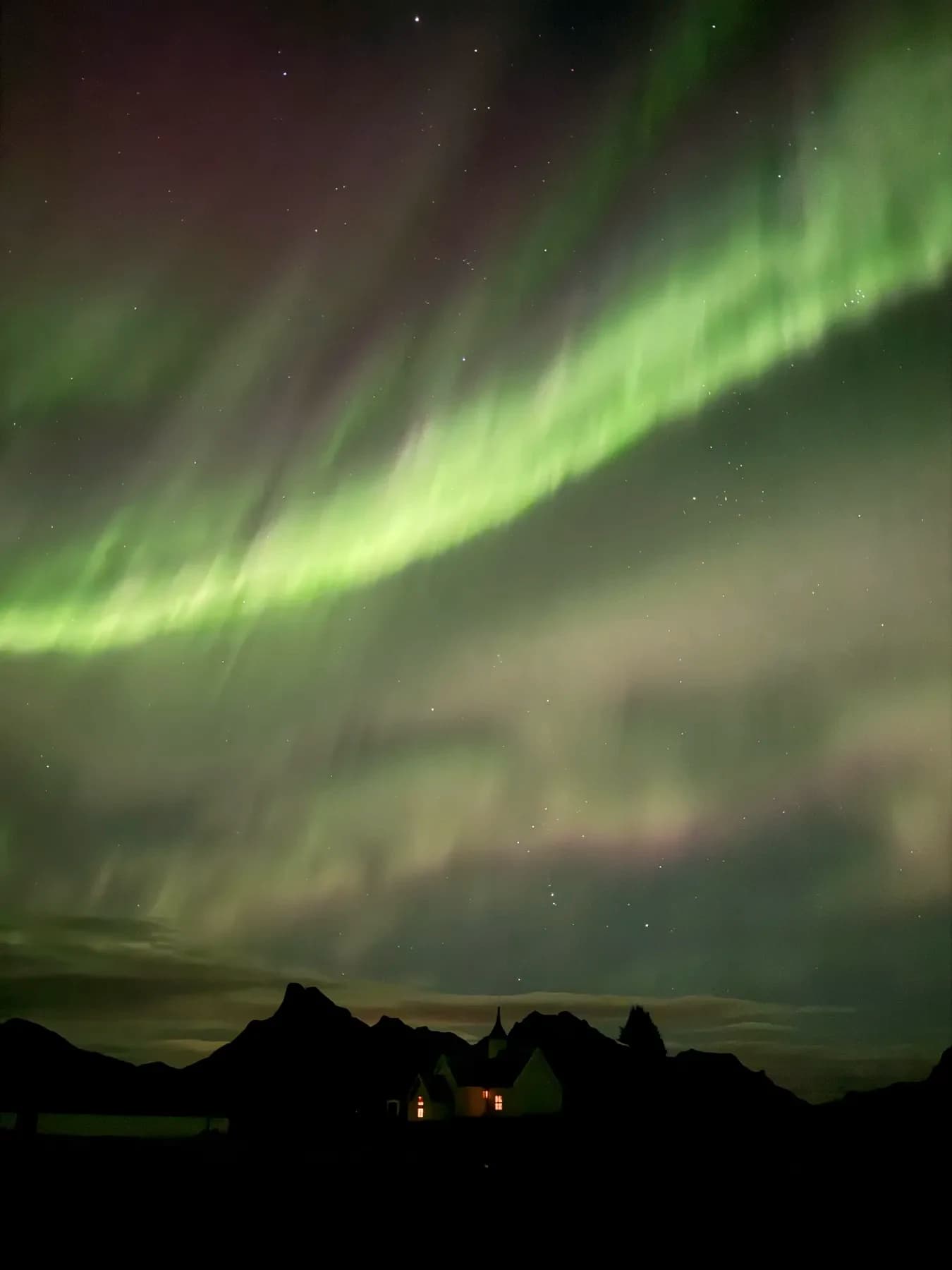 Nordlys over mørkt landskap med opplyst hus