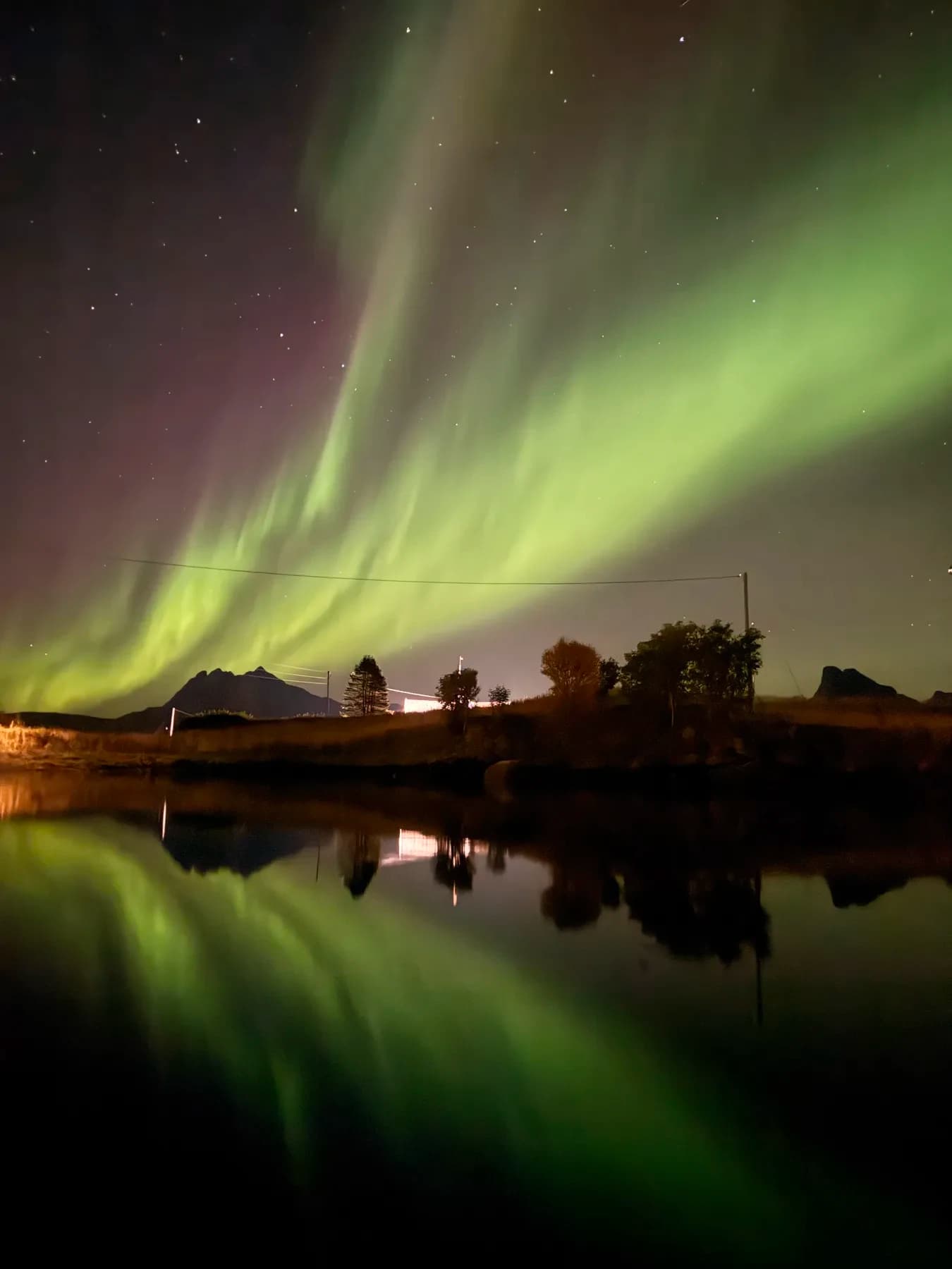 Nordlys speilet i stille vann med hus på land